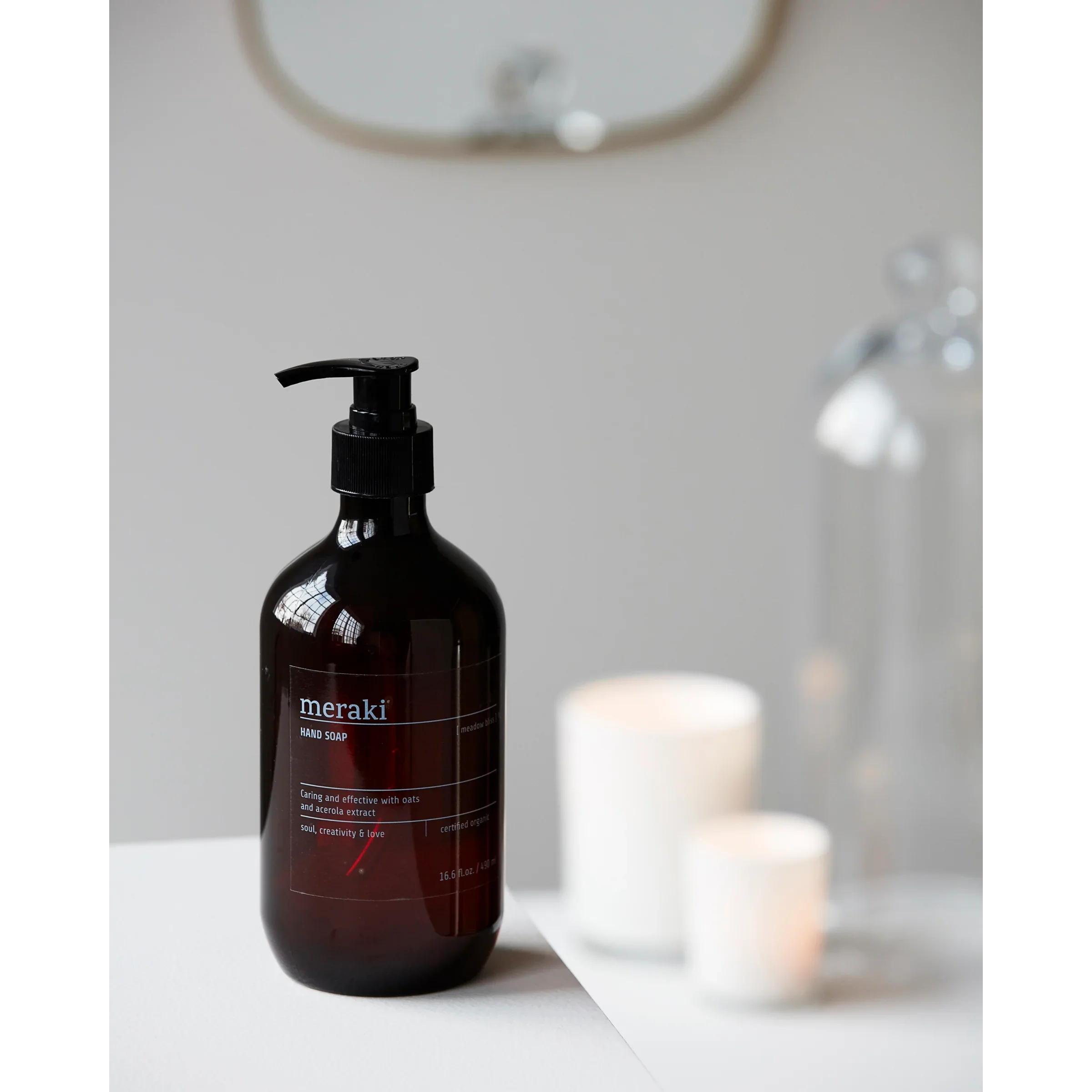 Meraki Meadow Bliss handzeep in donkere fles naast witte geurkaars en spiegel, gestyled in rustgevend interieur