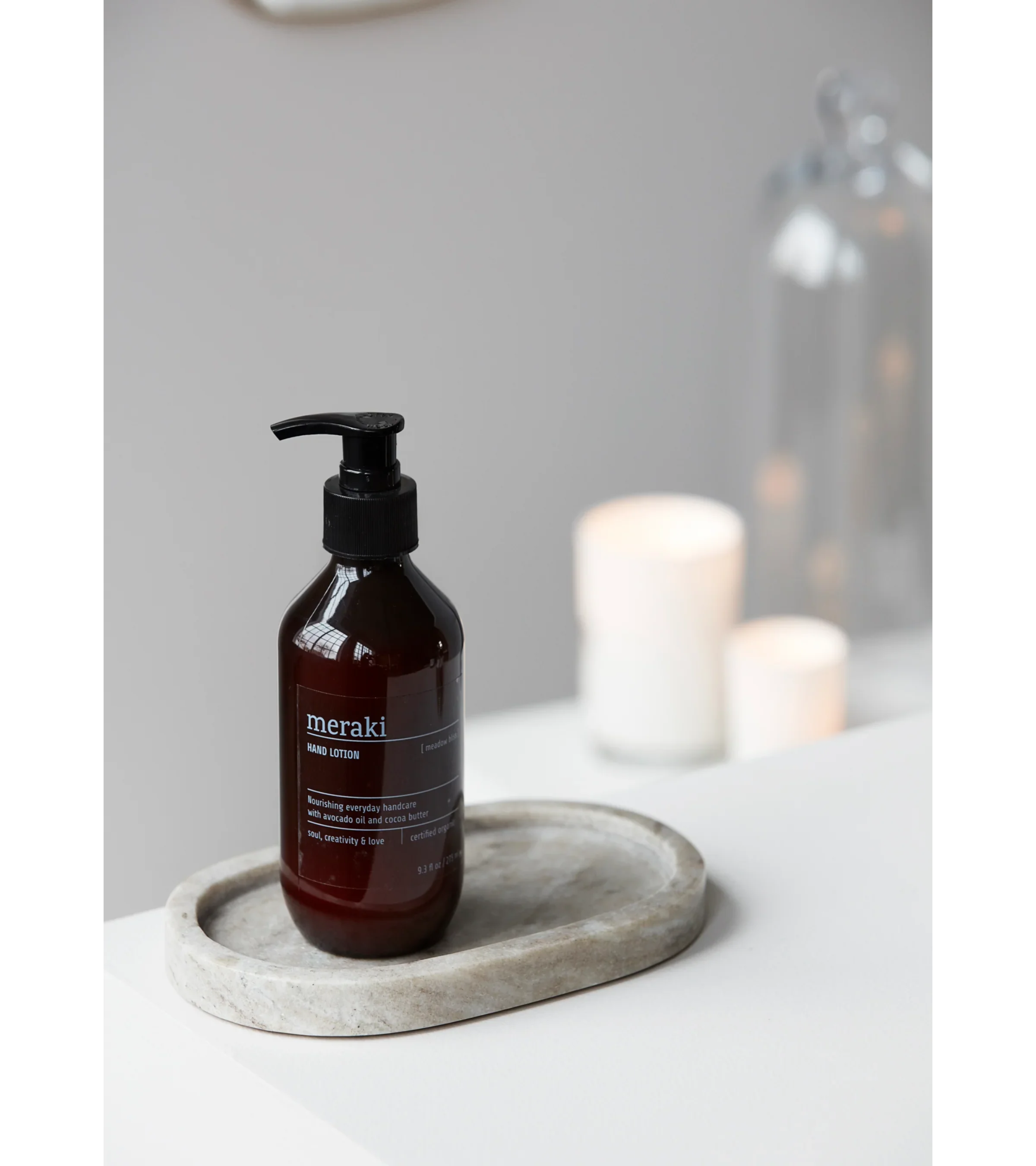 Meraki Meadow Bliss handlotion in donkerbruine fles met pomp, gestyled naast kaarsen op een marmeren ondergrond