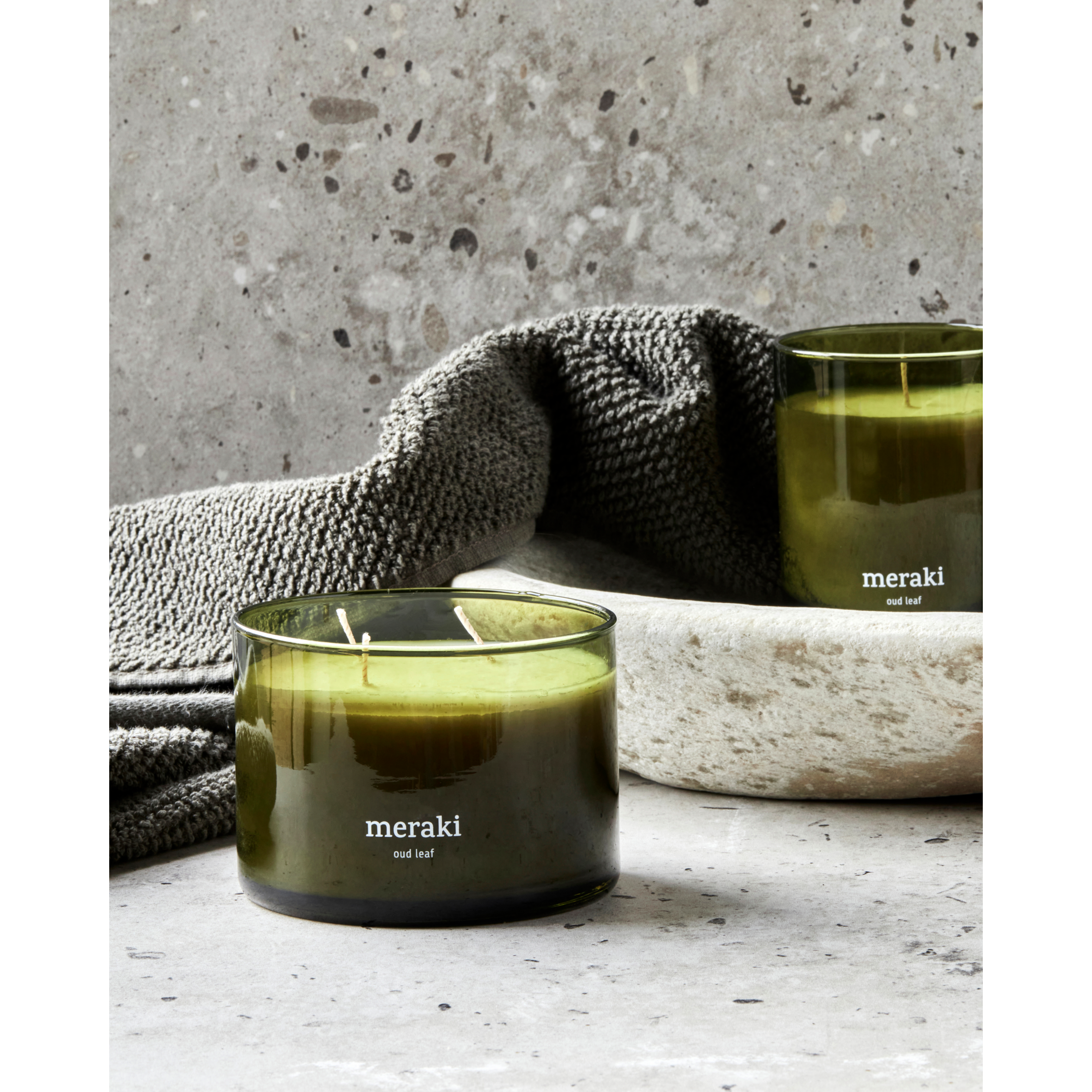 Groene Meraki geurkaars Oud Leaf met dubbele lont, gestyled op een stenen ondergrond met zachte handdoek – sfeervolle en luxe uitstraling.
