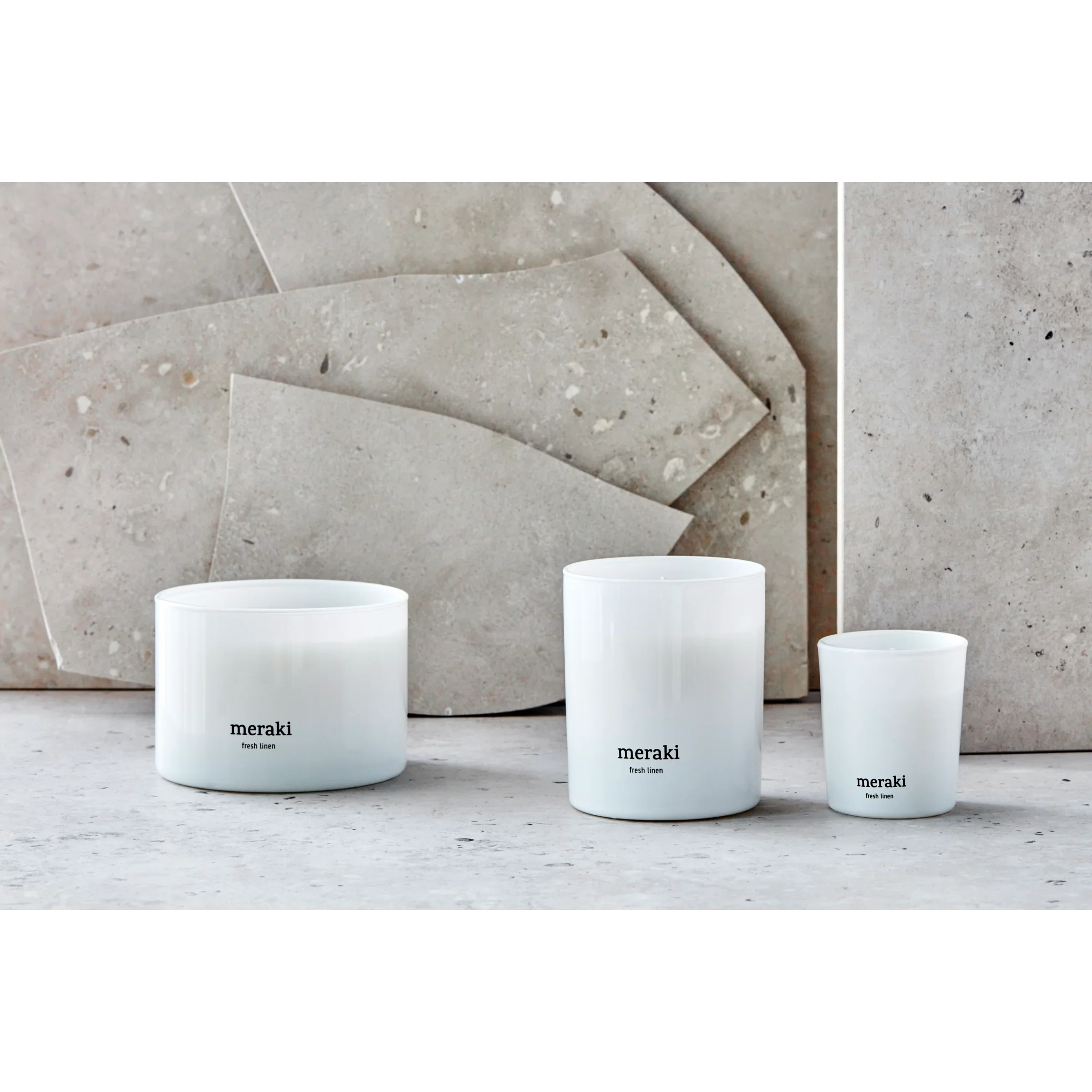 Meraki Fresh Linen geurkaarsen in drie formaten gestyled tegen een beige stenen achtergrond